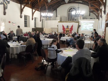 Members of the community are seated in small groups. They are asked to brainstorm ideas on paper and answer questions from the commissioners. (Photo: Melissa Shaw)