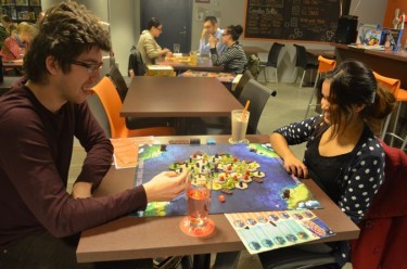 Nik Taylor and Shivangi Kaushik play a board game while having drinks